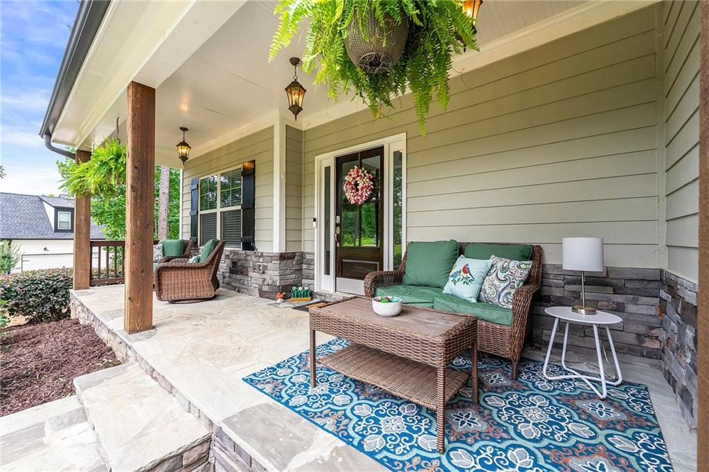 Covered porch with wicker seating, green cushions, hanging ferns, and a blue patterned rug.