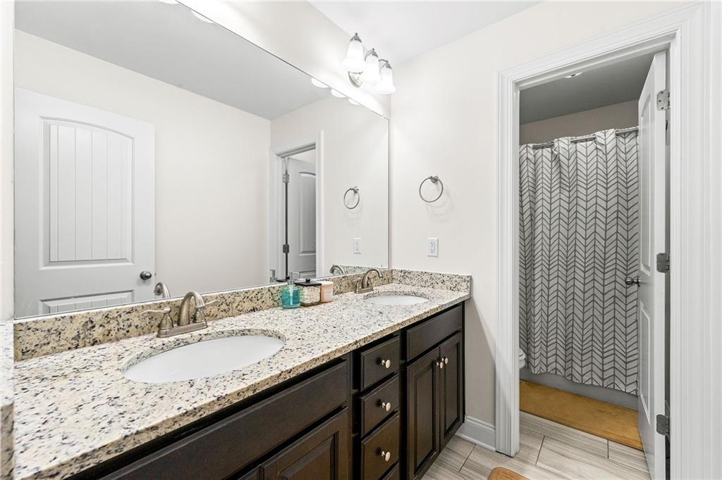 Bathroom with double-sink granite vanity, dark cabinetry, and a geometric-patterned shower curtain.