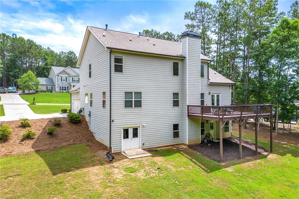 Rear exterior of a two-story house with a raised deck beside a wooded yard.