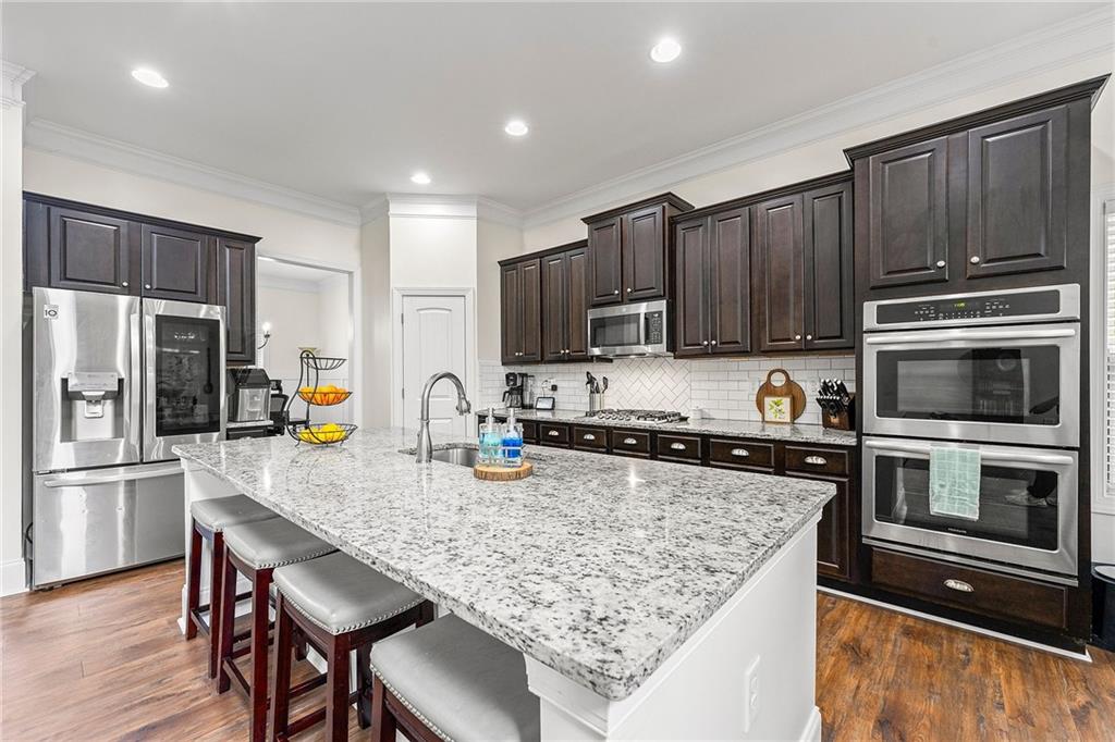 Kitchen with a large granite island, dark cabinetry, and stainless steel appliances.