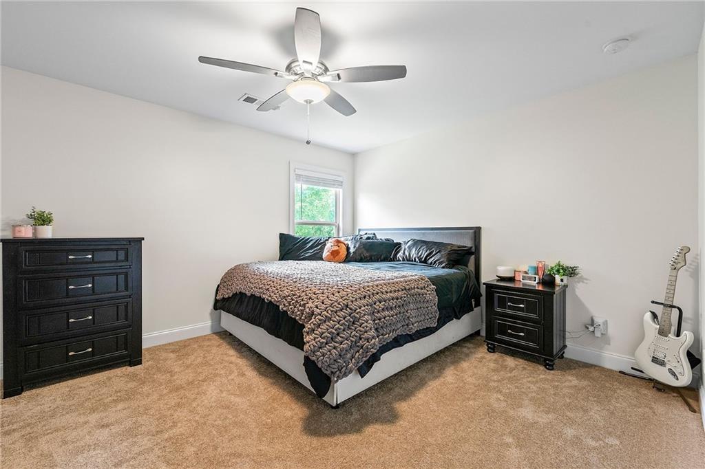 Bedroom with dark bedding, black dressers, a ceiling fan, and a white electric guitar.