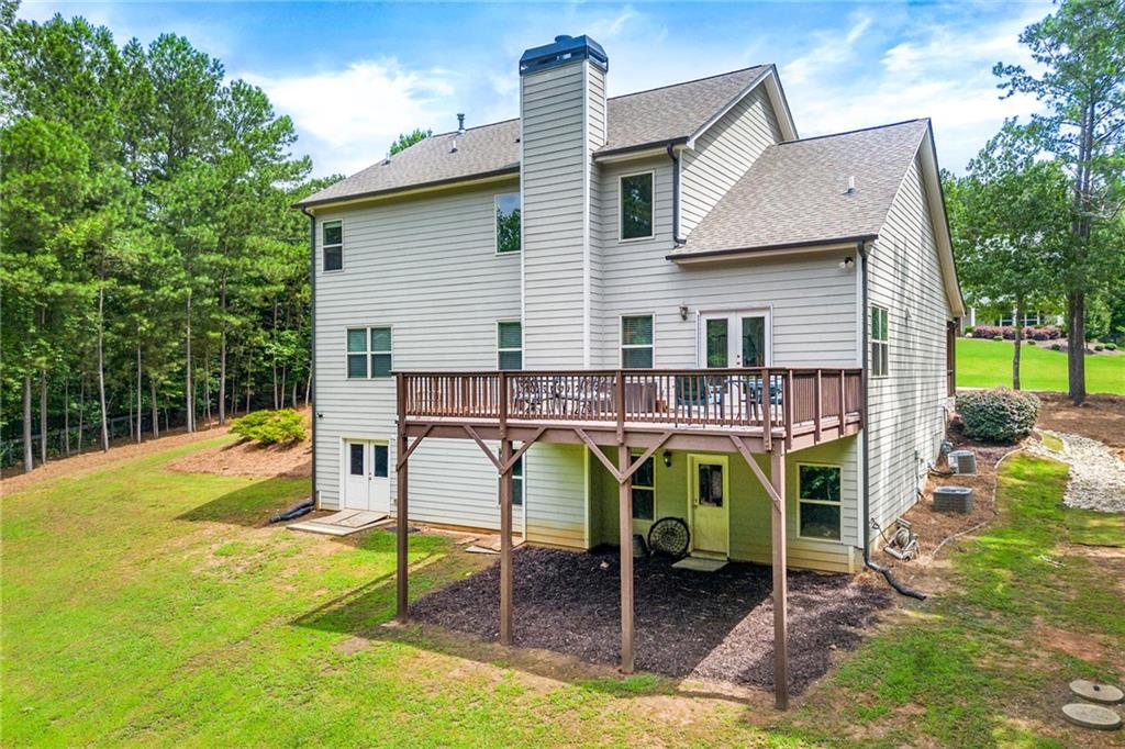 Rear of a two-story home with a raised wooden deck and tree-lined backyard.
