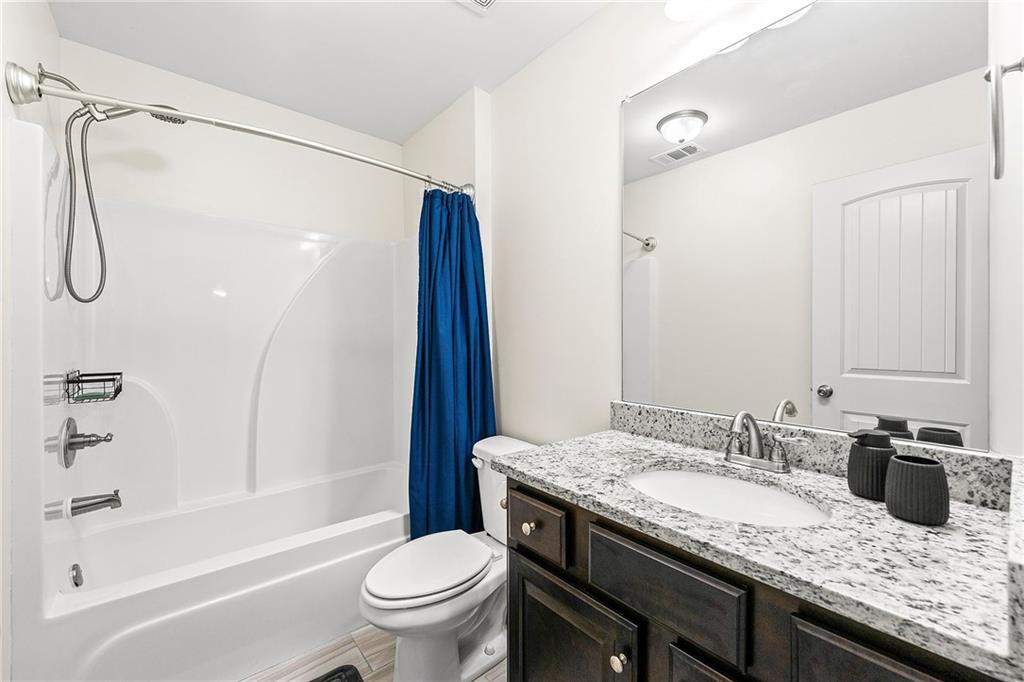 Bathroom with a blue shower curtain, white tub, and dark wood vanity with granite counter.