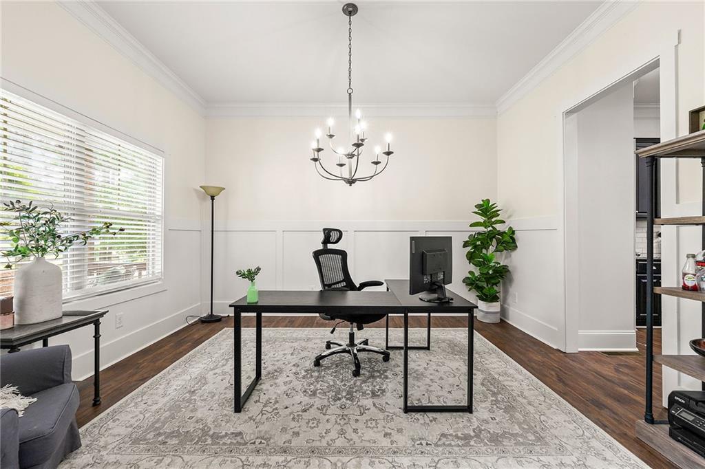 Home office with a black desk, patterned rug, white paneling, and wide window.