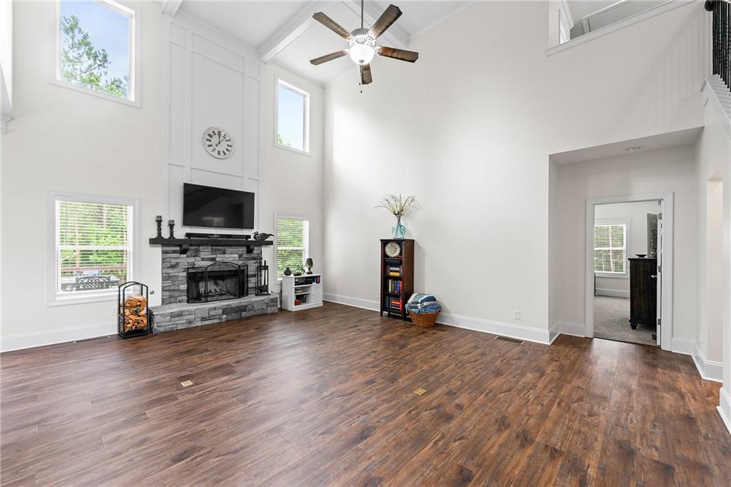 Living room with a stone fireplace, tall windows, and dark wood flooring beneath a vaulted ceiling.