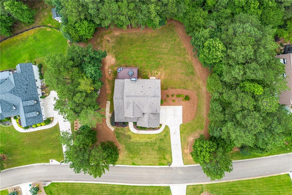 Aerial view of a house on a wooded lot with a curved driveway and neighboring homes.