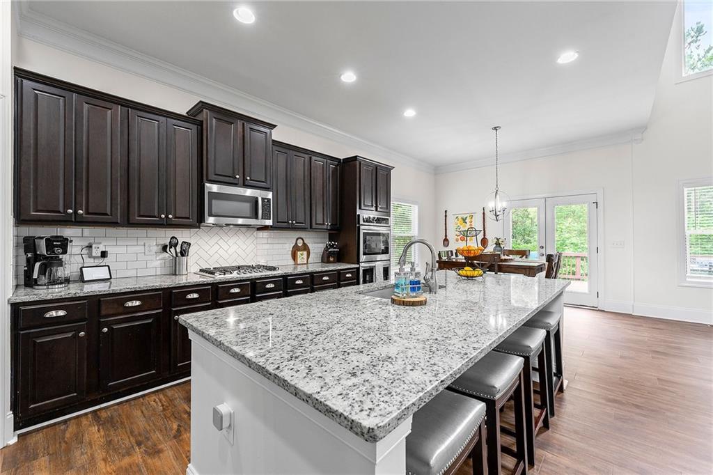 Kitchen with dark wood cabinets, stainless appliances, and a large granite island with bar stools.