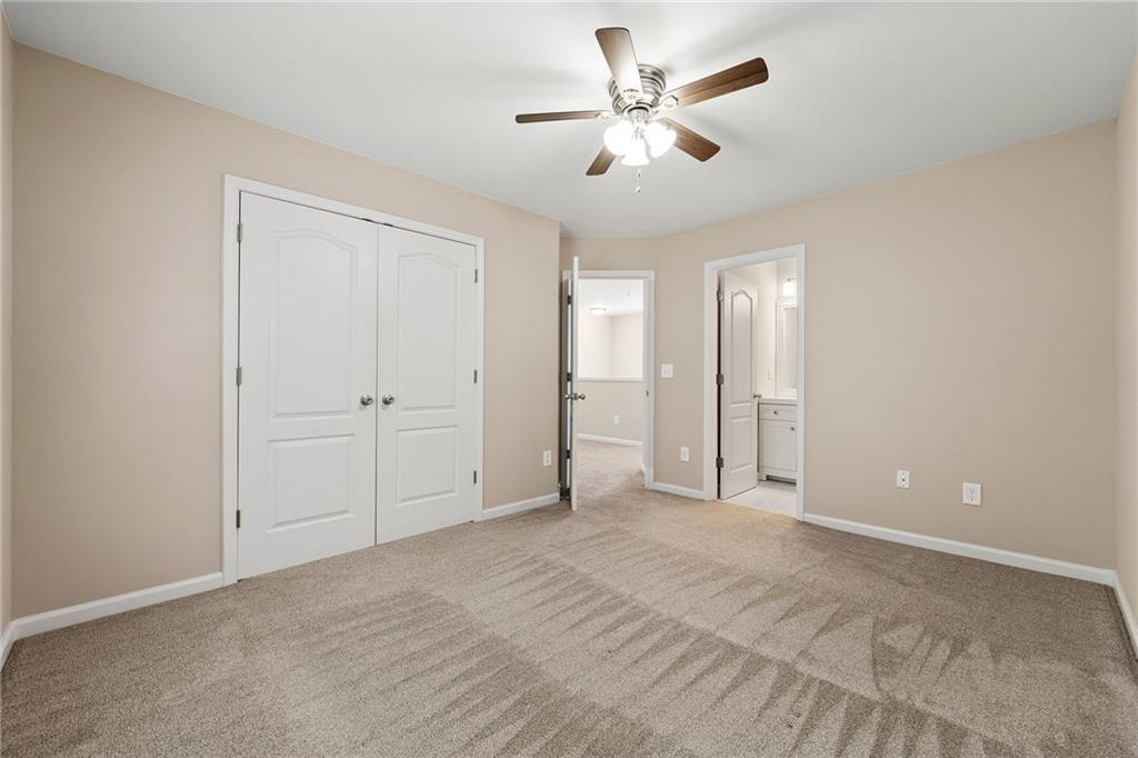 Empty bedroom with tan carpet, double closet doors, and a ceiling fan with light.