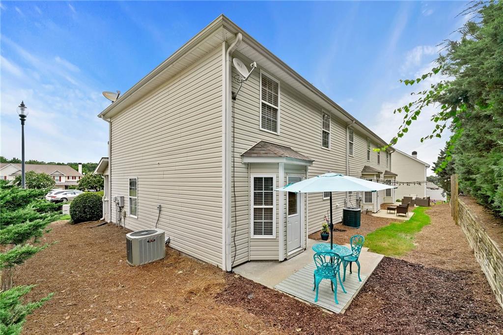 Rear of a beige two-story home with a patio, turquoise chairs, and a blue umbrella.