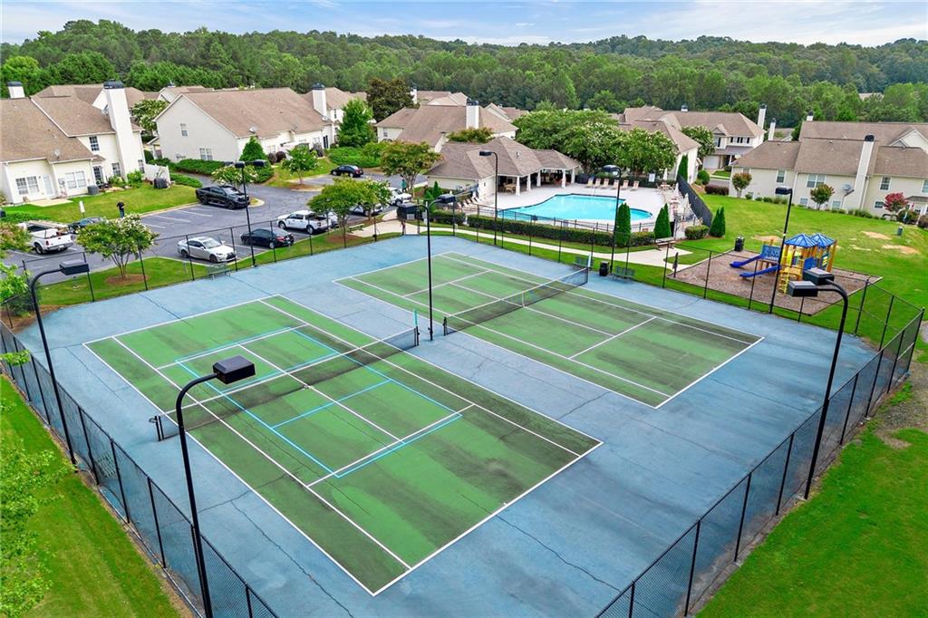 Two fenced tennis courts overlook a community pool, playground, and surrounding homes.