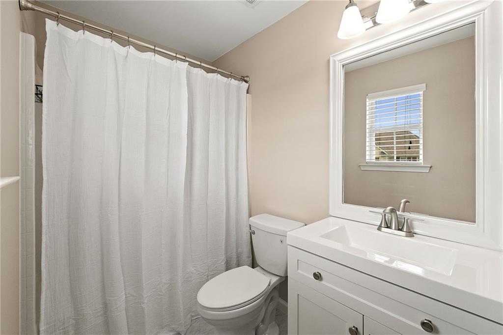 Bathroom with a white shower curtain, toilet, and vanity beneath a large framed mirror.