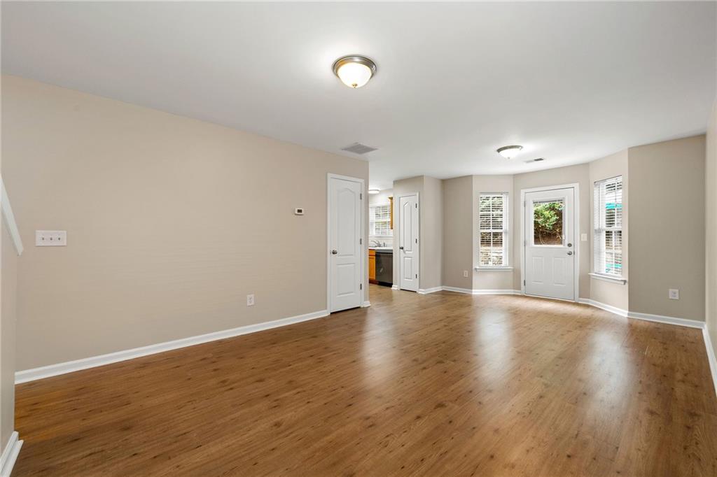 Empty room with hardwood floors, beige walls, and a white exterior door flanked by windows.
