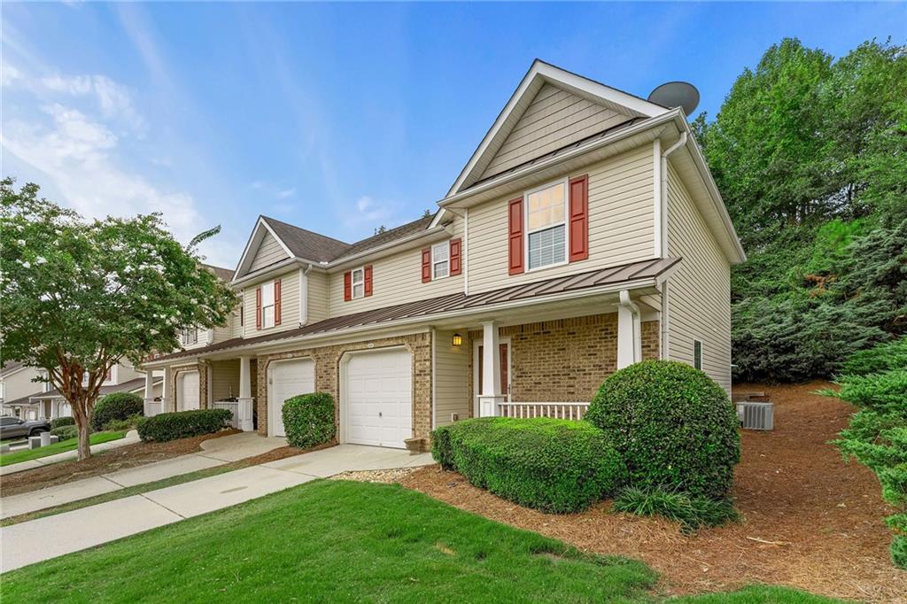 Townhouse exterior with brick lower facade, red shutters, attached garage, and landscaped lawn.