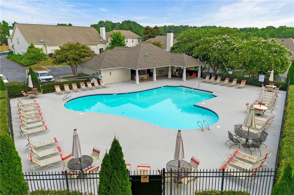 Community swimming pool surrounded by lounge chairs, with a covered pavilion and homes beyond.