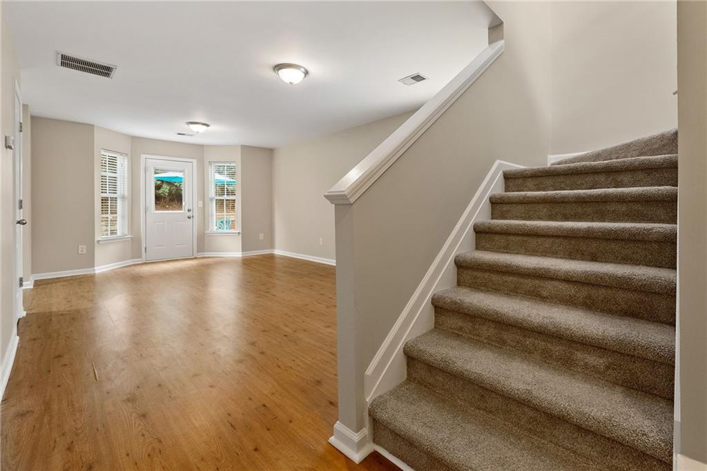 Empty foyer with hardwood floors, a windowed front door, and a carpeted staircase.