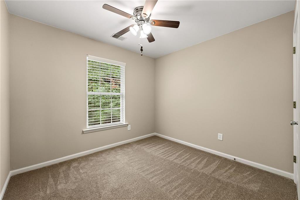 Vacant bedroom with beige walls, carpet, a window with blinds, and a ceiling fan.