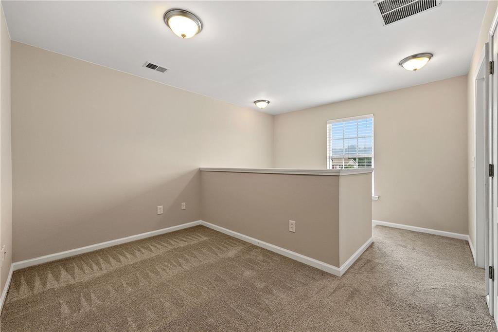 Carpeted upstairs loft with a half-height partition and a window with blinds.