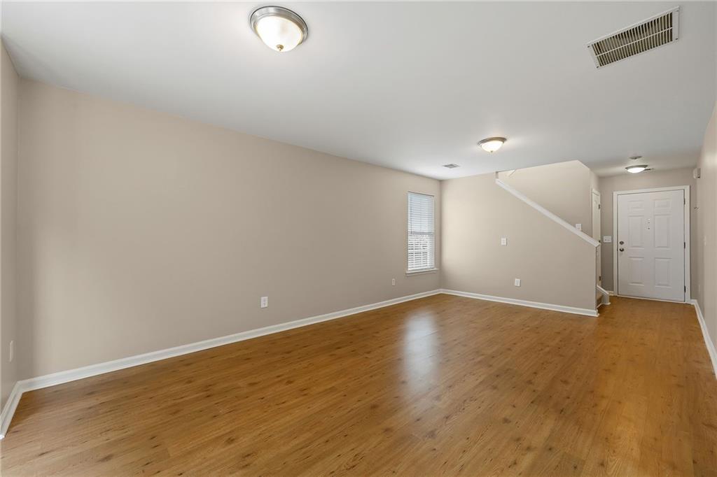 Empty living room with hardwood floors, a staircase, and a white front door.