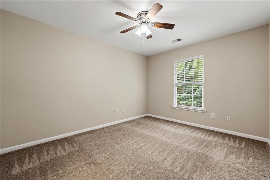 Empty bedroom with patterned carpet, a ceiling fan, and a window with white blinds.