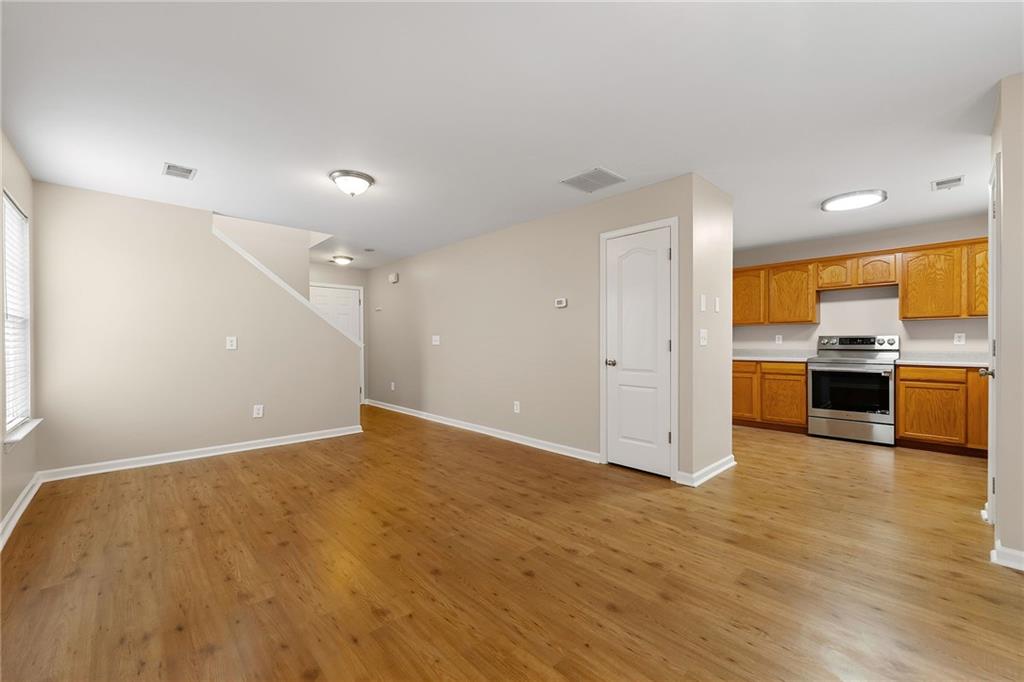 Open living area with hardwood floors and adjoining kitchen with oak cabinets and stainless appliances.