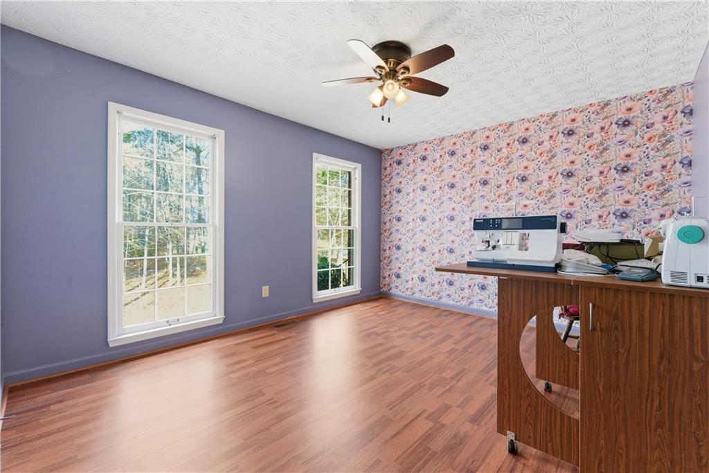 Sewing room with floral wallpaper, lavender walls, hardwood floors, and two tall windows.