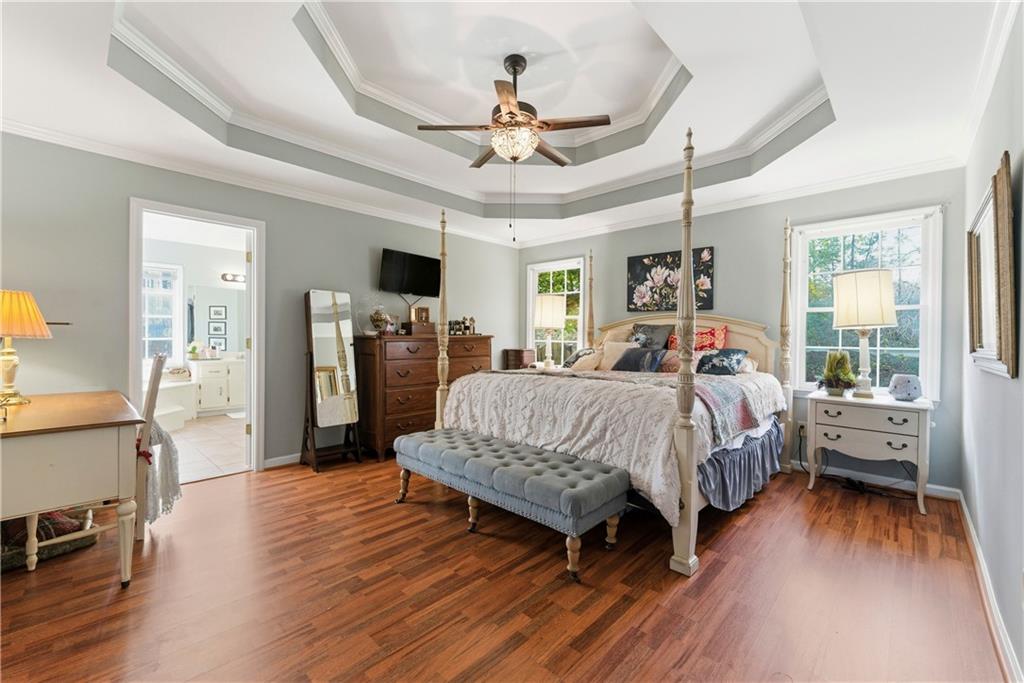 Primary bedroom with a four-poster bed, hardwood floors, and a layered tray ceiling.