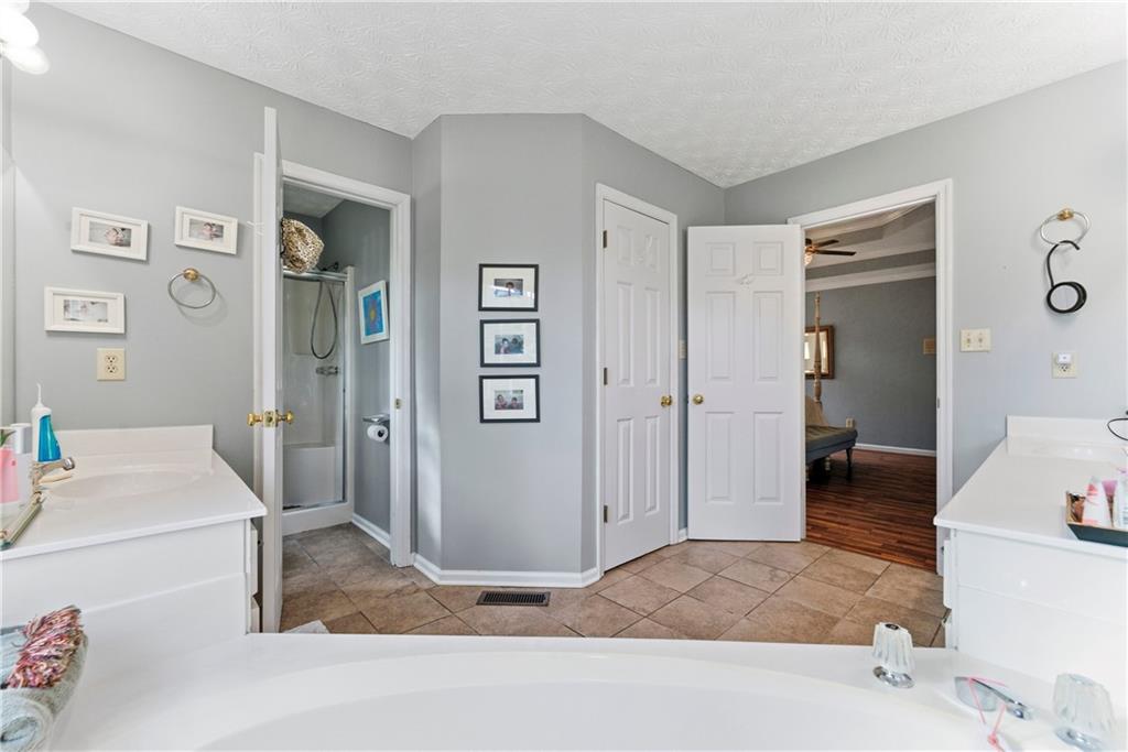 Bathroom with a large white bathtub, tiled floor, and glass-enclosed shower beside an open bedroom doorway.