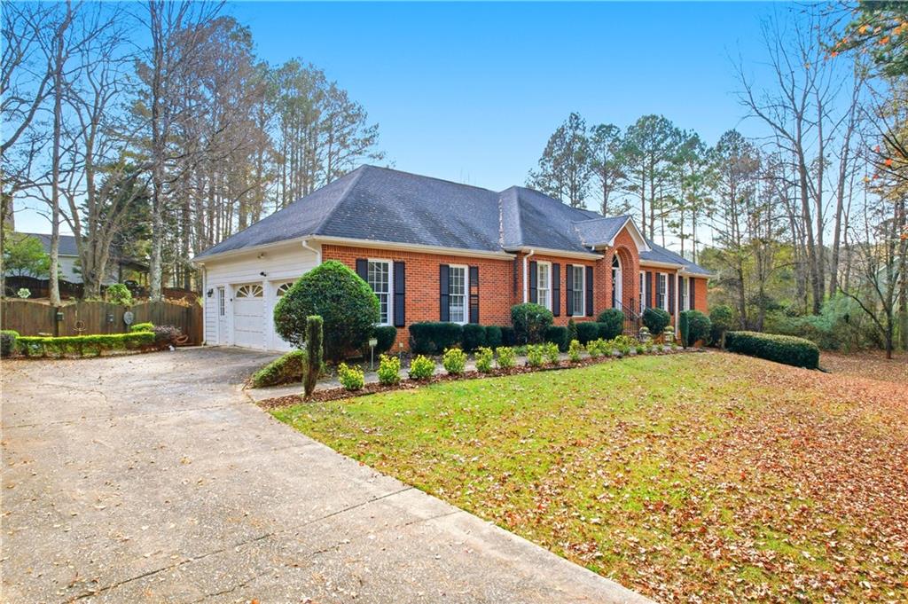 Red brick home with an attached garage, wide driveway, trimmed landscaping, and leaf-covered lawn.
