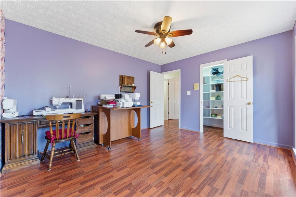 Sewing room with multiple machines, worktables, purple walls, and hardwood floors.