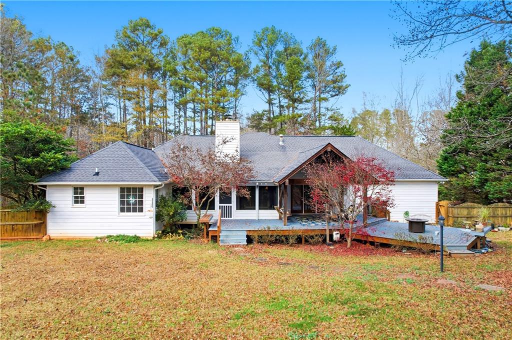 Rear of a white house with a covered wooden deck and fenced, tree-lined backyard.
