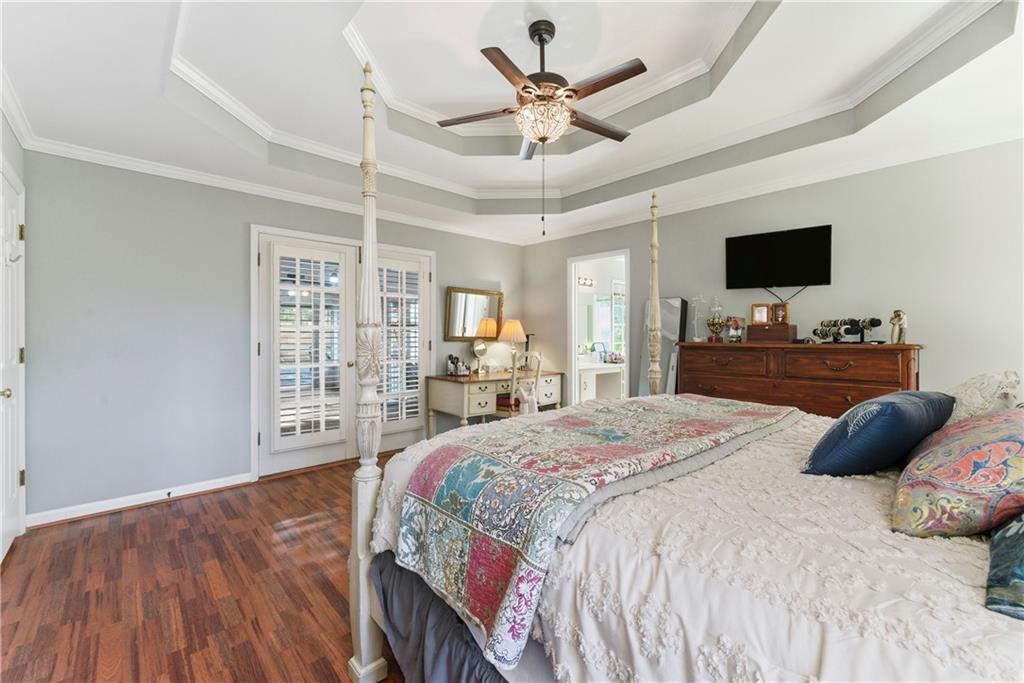 Bedroom with a four-poster bed, hardwood floors, shuttered French doors, and a tray ceiling.