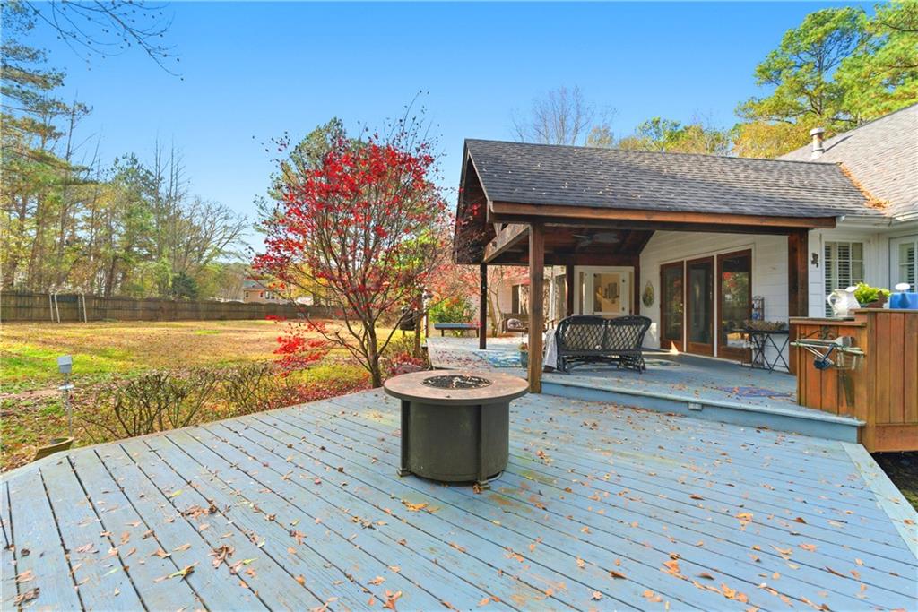 Backyard deck with a round fire pit, covered patio, outdoor seating, and red-leaved tree.