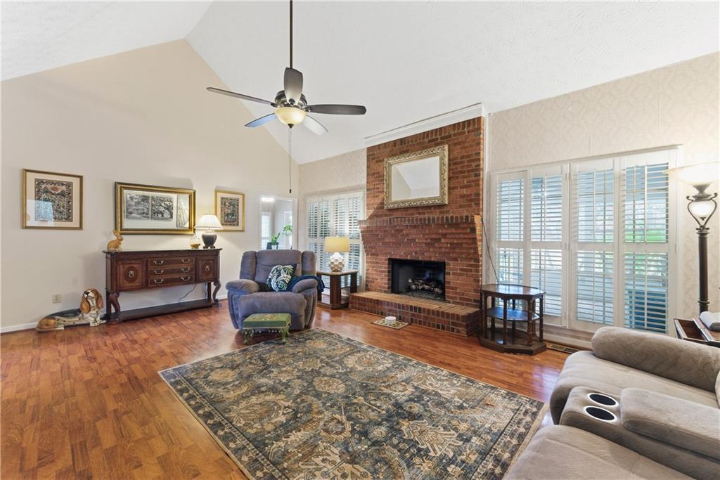 Living room with a brick fireplace, hardwood floors, and plantation shutters.