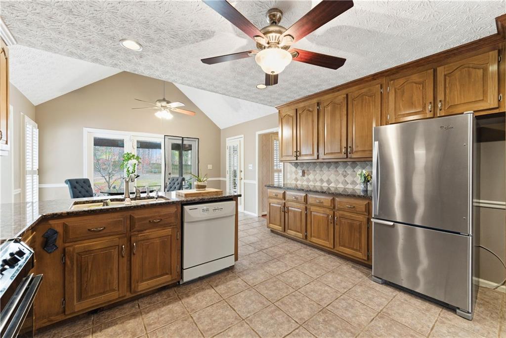 Kitchen with warm wood cabinets, stainless steel refrigerator, and island opening to a dining area.