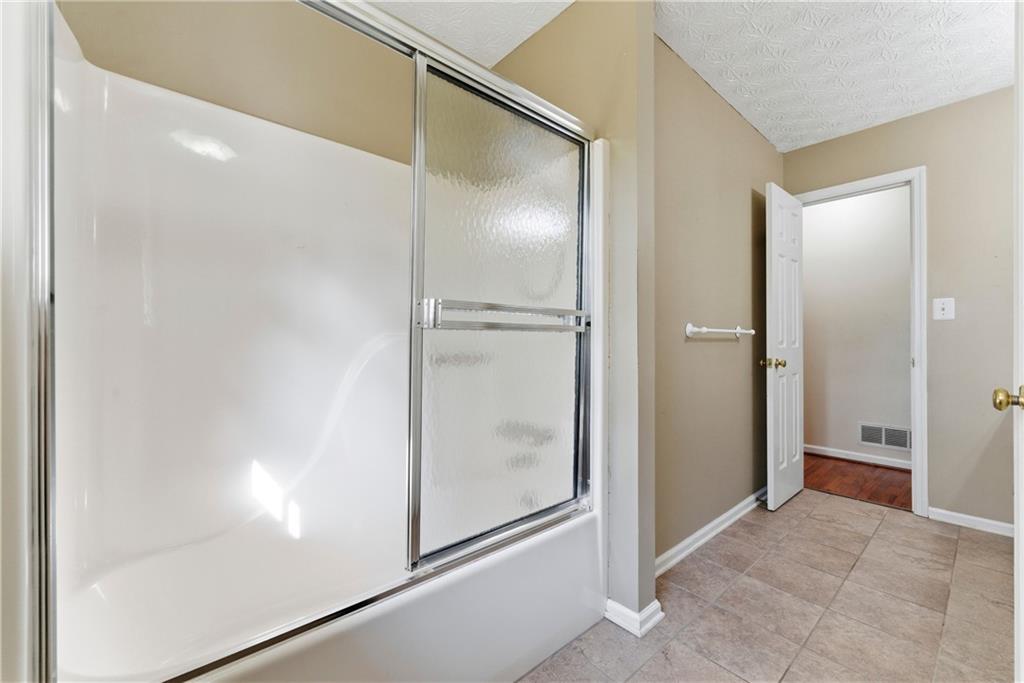 Bathroom with a white tub and sliding textured-glass shower door beside a tiled floor.