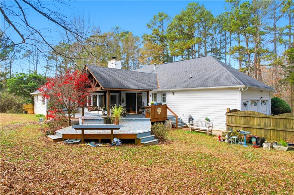 Rear of a white home with a raised deck and fenced, leaf-covered backyard.