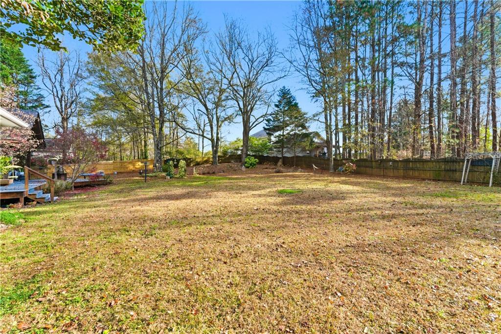 Spacious fenced backyard with mature trees, a wooden deck, and a metal play structure.