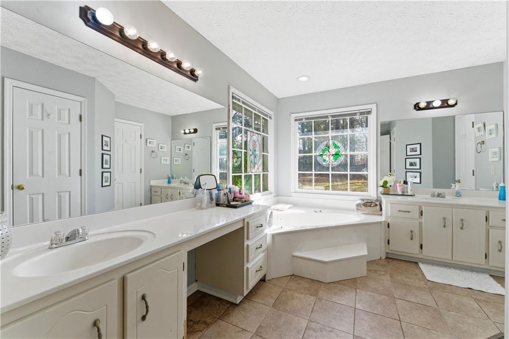 Bright bathroom with a long double vanity and soaking tub beneath large windows.