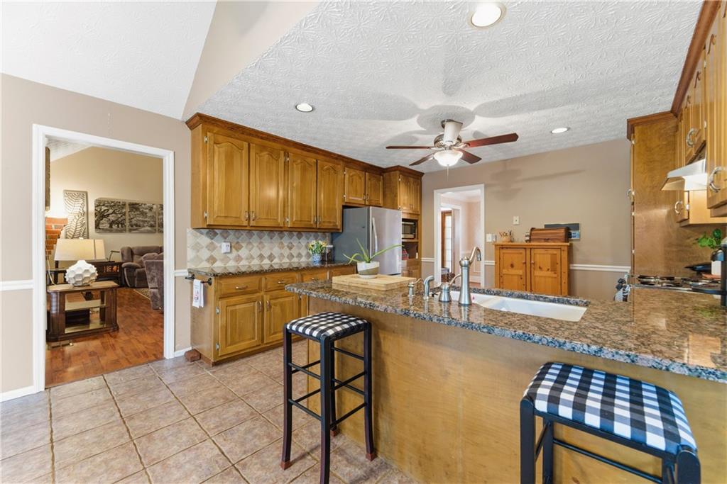 Kitchen with honey-colored cabinets, granite peninsula, white sink, and two checkered stools.