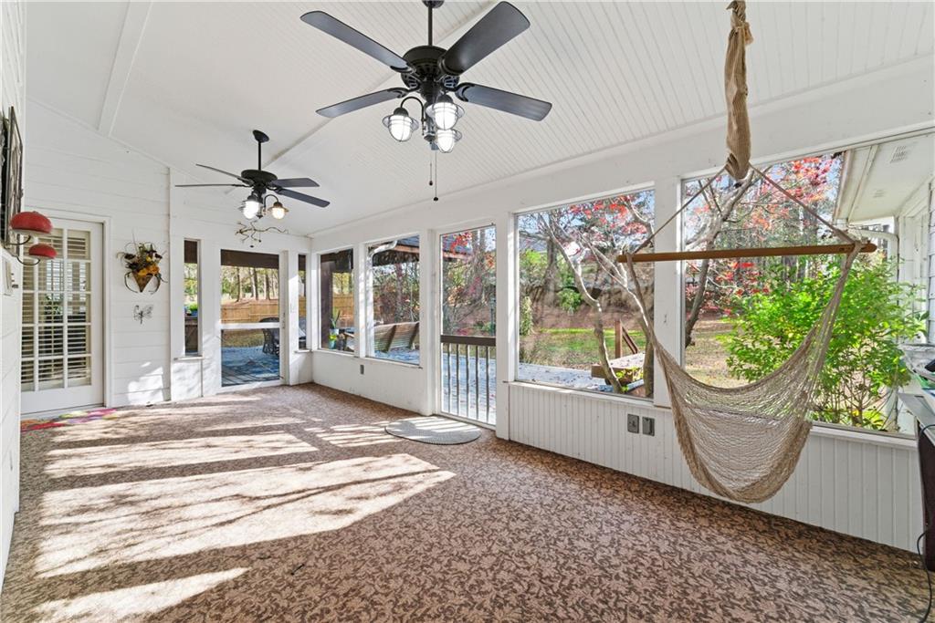Enclosed sunroom with large windows, two ceiling fans, and a hanging hammock overlooking a wooded yard.