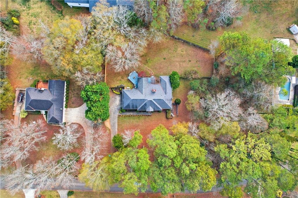 Aerial view of a house on a wooded lot, with a driveway and neighboring homes.