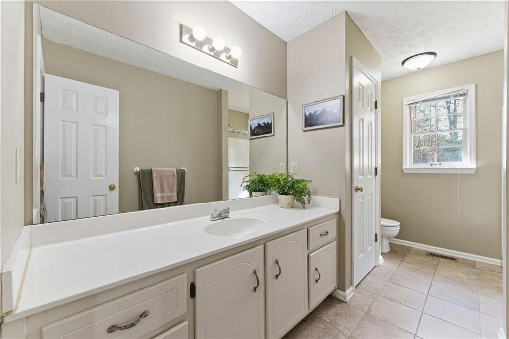 Bathroom with a long white vanity, large mirror, tiled floor, and window overlooking trees.