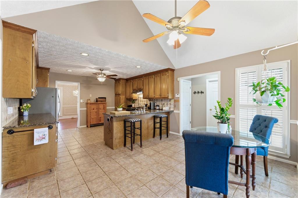 Open kitchen with wood cabinets, central island and bar stools, adjoining a dining area with blue chairs.