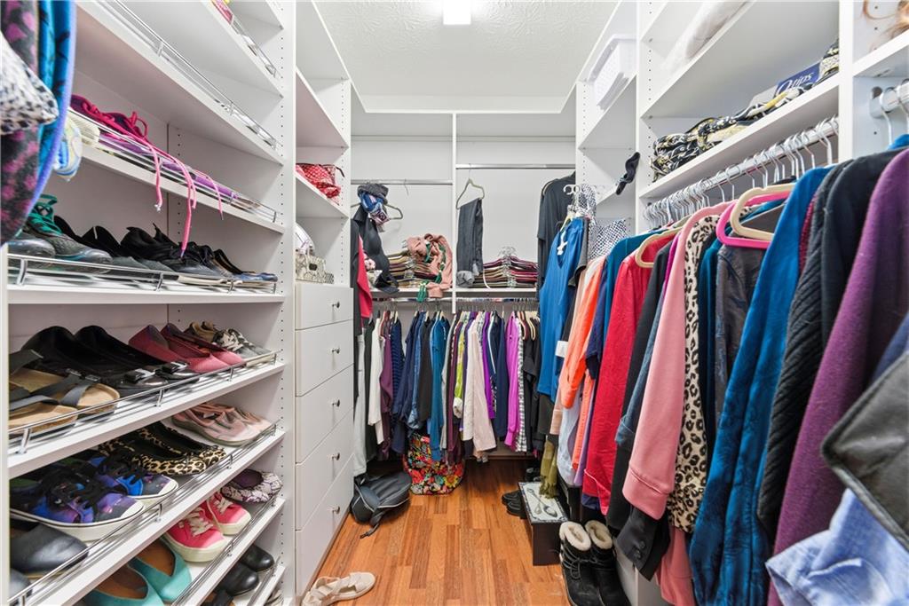 Walk-in closet with built-in shoe shelves, drawers, and clothing on multiple hanging rods.