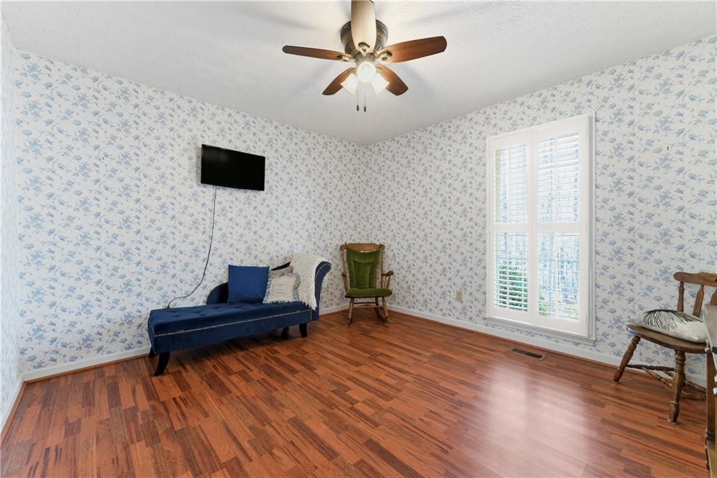 Furnished room with floral wallpaper, a blue chaise lounge, hardwood floors, and a tall shuttered window.