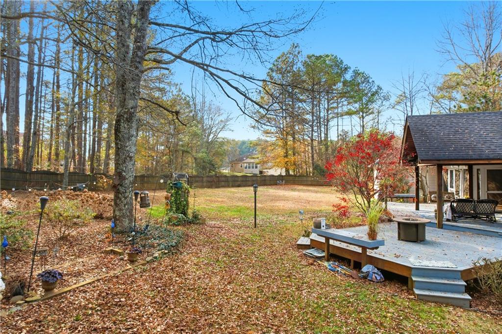 Fenced backyard with a raised deck, outdoor seating, and mature autumn trees.