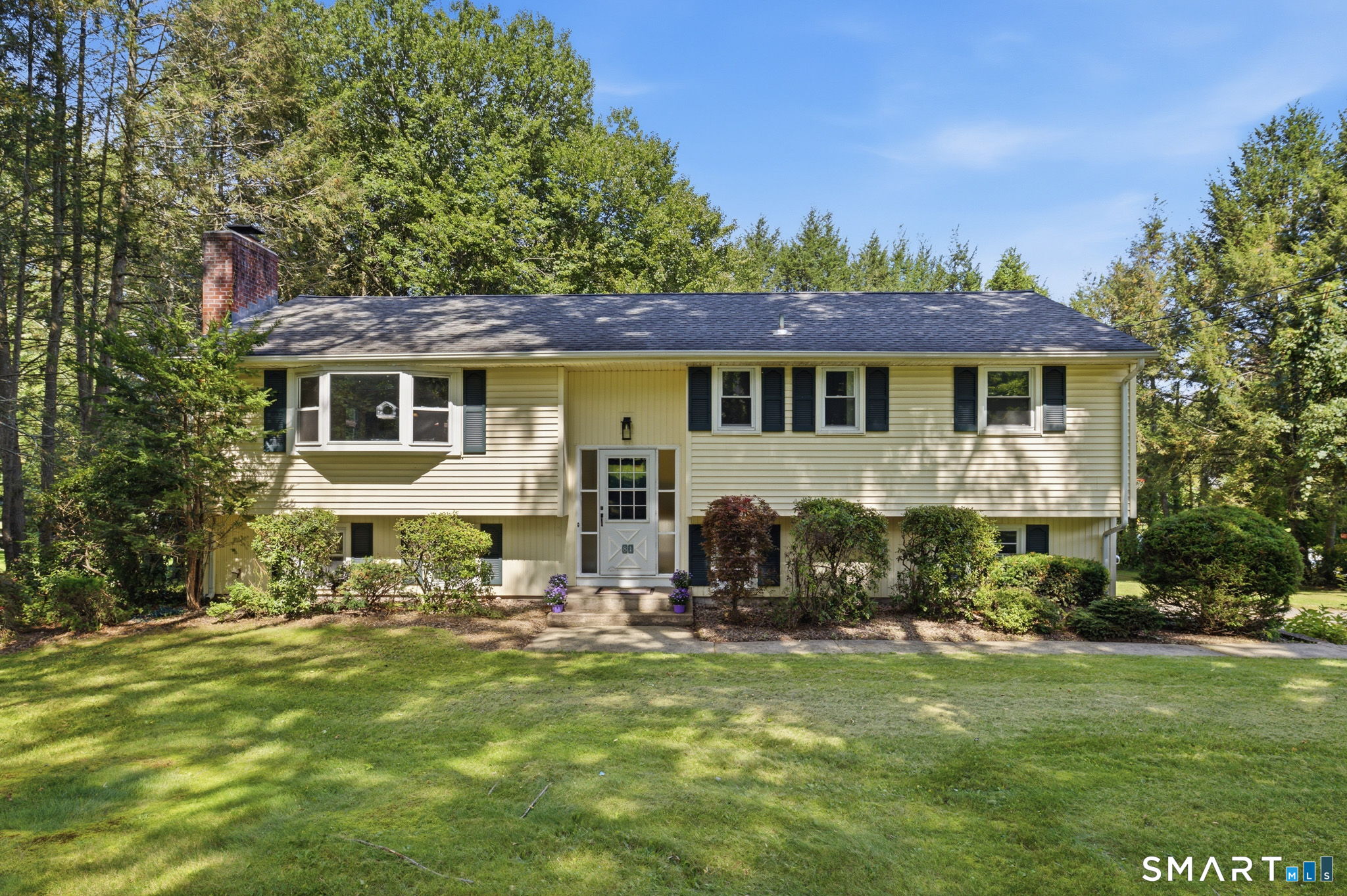 Pale yellow split-level home with a projecting bay window, brick chimney, and broad green lawn.