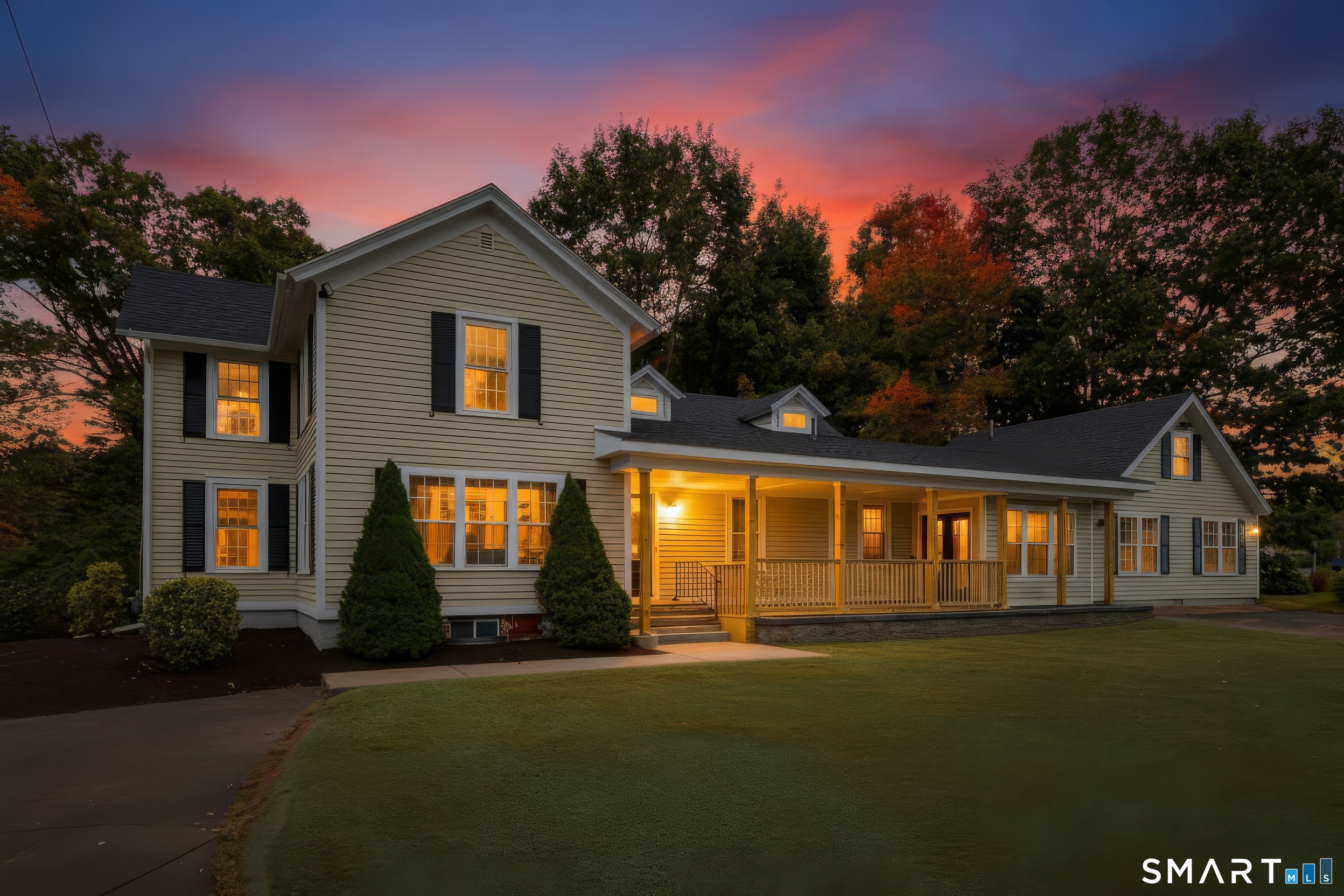 Two-story house with a long covered porch and warmly lit windows at dusk.