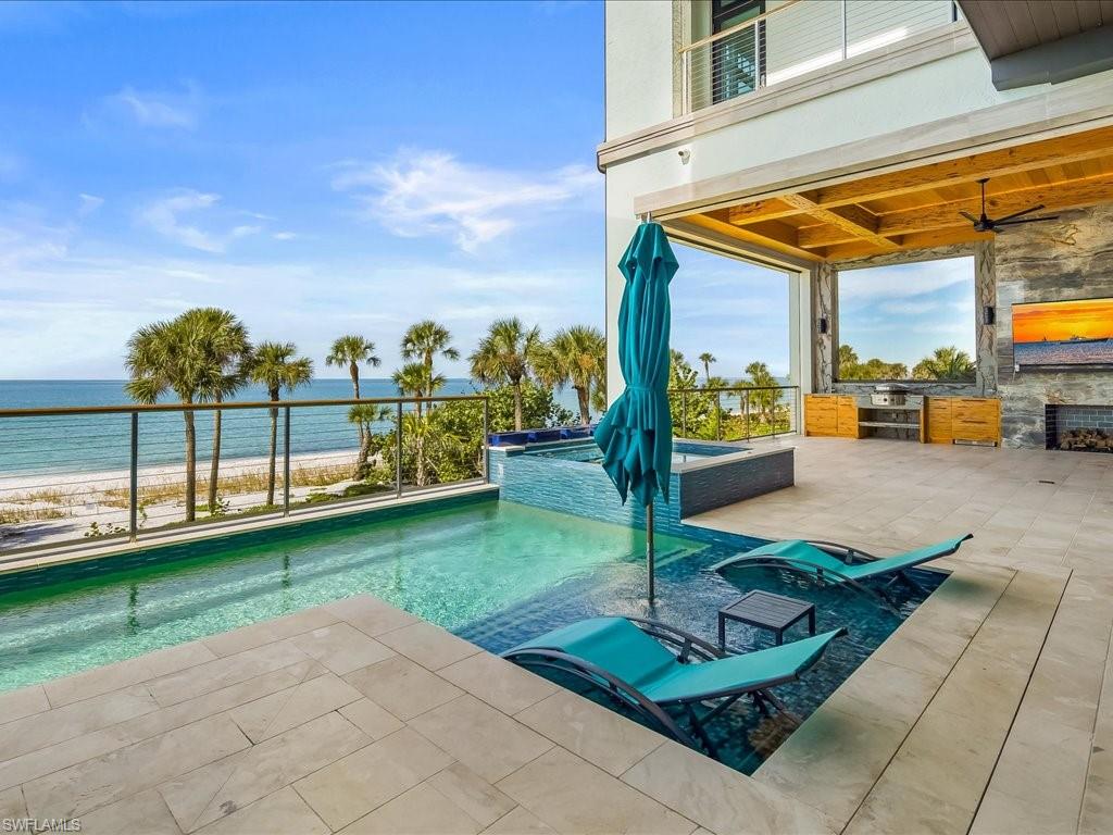 Oceanfront pool and spa beside a covered outdoor kitchen, with palm trees and beach beyond.