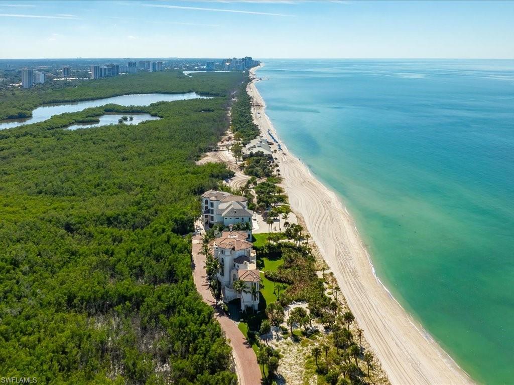 Aerial view of beachfront homes beside a long sandy beach and turquoise Gulf water.